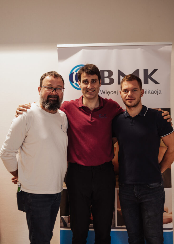 Three men stand in front of a sign for BMK organization.